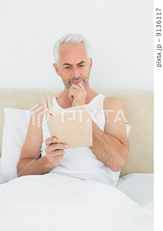 Relaxed mature man reading book in bed 9136117