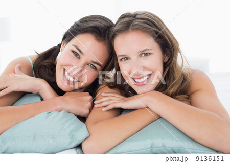 Two smiling young female friends lying in bed 9136151