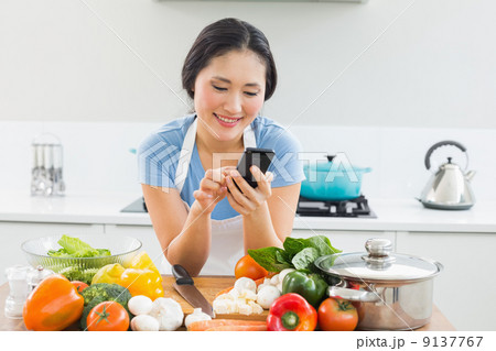 Woman text messaging in front of vegetables in kitchen 9137767