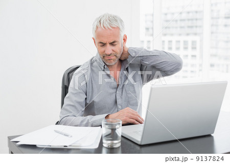 Man suffering from neck ache while using laptop at office desk Man suffering from neck ache while using laptop at office desk 9137824