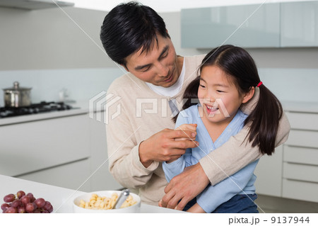 Cheerful father with daughter having cereals in kitchen 9137944