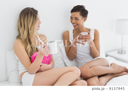 Relaxed female friends with coffee cups in bed 9137945