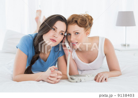 Beautiful woman with friend using phone in bed Beautiful woman with friend using phone in bed 9138403