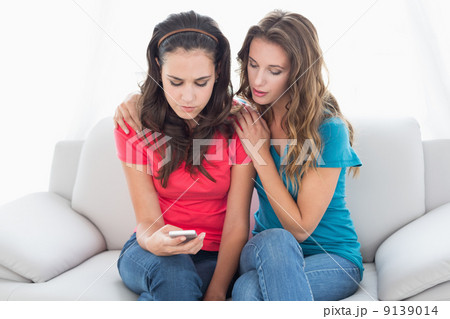 Upset female friends reading text message at home Upset female friends reading text message at home 9139014