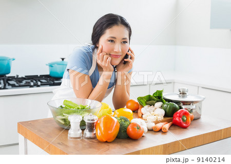 Woman using mobile phone in front of vegetables in kitchen 9140214