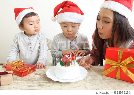 クリスマスケーキのロウソクの火を吹き消す家族の写真素材