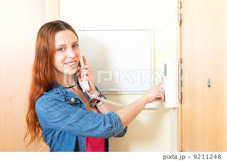 Young woman talking on the house videophone indoor Young woman talking on the house videophone indoor 9211248