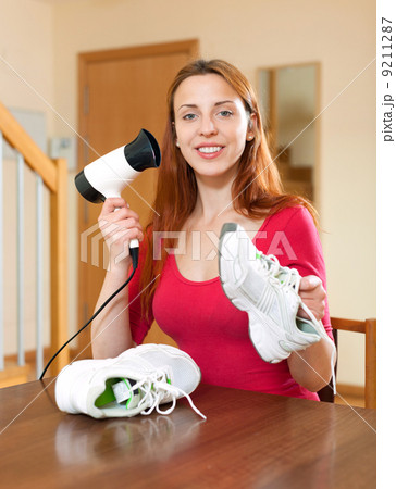 Girl dries the running shoes with hair dryer Girl dries the running shoes with hair dryer 9211287