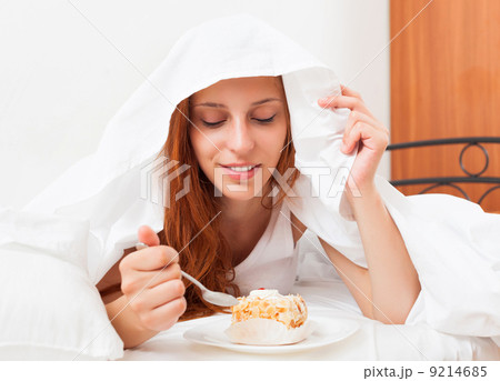 woman eating sweet cake under in bed 9214685