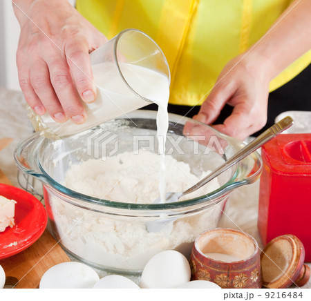 cook hands pouring milk into flour 9216484