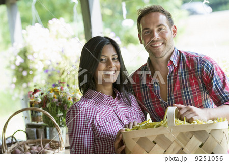 A farm stand with fresh organic vegetables and fruit.  A man and woman with baskets of beans.  9251056