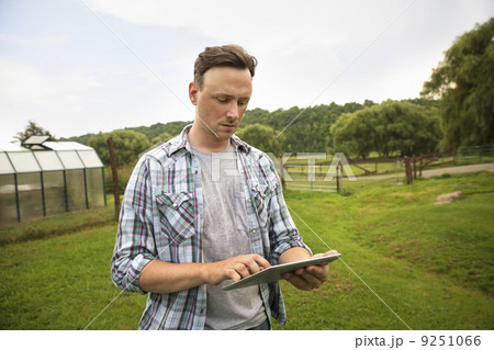 An organic farm in the Catskills. A man using a digital tablet in a grass paddock. An organic farm in the Catskills. A man using a digital tablet in a grass paddock. 9251066