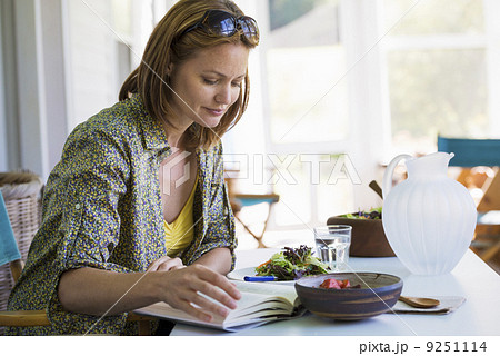 A woman sitting at a table reading a book.  9251114