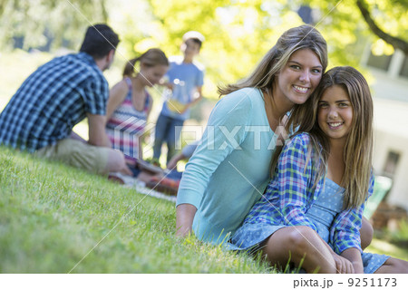 A group of adults and children sitting on the grass under the shade of a tree. A family party. A group of adults and children sitting on the grass under the shade of a tree. A family party. 9251173