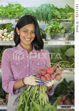 A farm stand with rows of freshly picked vegetables for sale. A woman holding a bunch of carrots.  9251181
