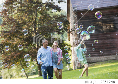 A family sitting on the grass outside a bar, blowing bubbles and laughing. 9251240