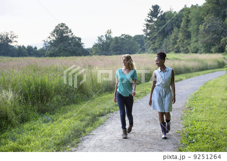 Two women walking down a path lined with trees. Two women walking down a path lined with trees. 9251264