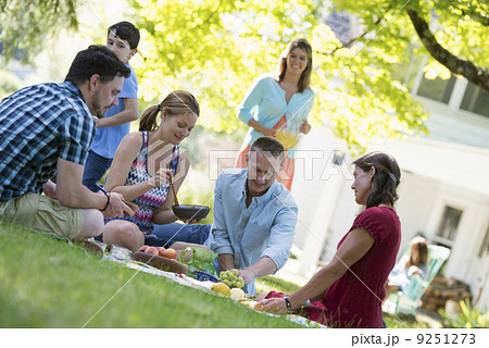 A group of adults and children sitting on the grass under the shade of a tree. A family party. A group of adults and children sitting on the grass under the shade of a tree. A family party. 9251273