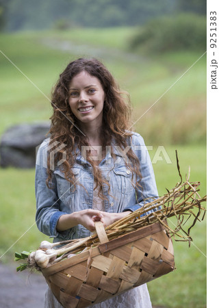 A young woman carrying a basket of freshly harvested garlic and vegetables. A young woman carrying a basket of freshly harvested garlic and vegetables. 9251383