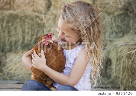 A young girl holding a chicken in a henhouse. 9251426