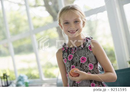 A young girl in a floral dress holding a peach fruit.  9251595