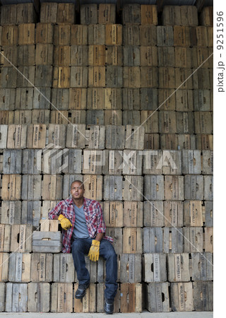 A farmyard. A stack of traditional wooden crates for packing fruit and vegetables. A man sitting on a packing case. 9251596