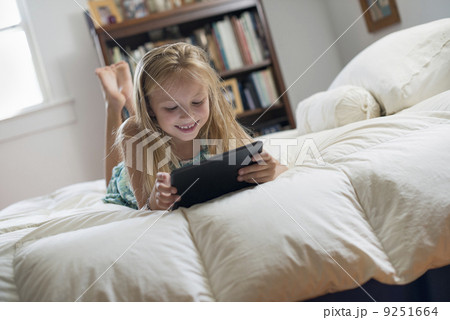 A young girl sitting on her bed using a digital tablet. A young girl sitting on her bed using a digital tablet. 9251664