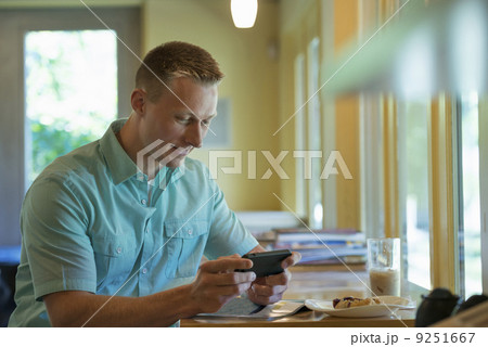 A man with short cropped hair sitting at a cafe table, using a smart phone. 9251667