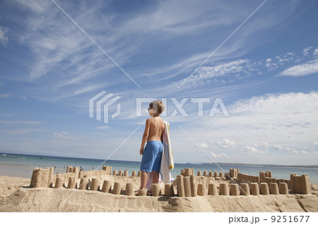 A boy standing beside a sandcastle, on top of a mound of sand. Beach. A boy standing beside a sandcastle, on top of a mound of sand. Beach. 9251677