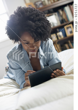 A woman lying on a bed, using a digital tablet. A woman lying on a bed, using a digital tablet. 9251727
