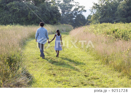 A man and a young girl walking down a mown path in the long grass holding hands.  9251728