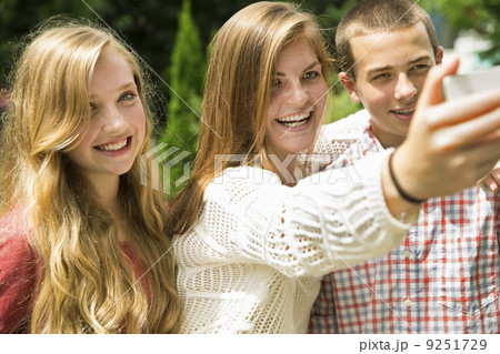 Three young people, two girls and a boy, posing and taking selfy photographs.  9251729