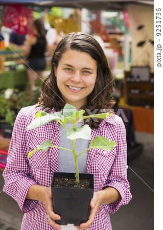 A young woman holding a small plant in a pot. Farm stand. A young woman holding a small plant in a pot. Farm stand. 9251736