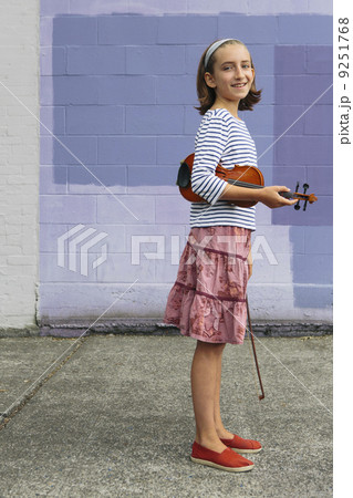 A ten year old girl holding a violin under her arm and a bow in her hand.  9251768