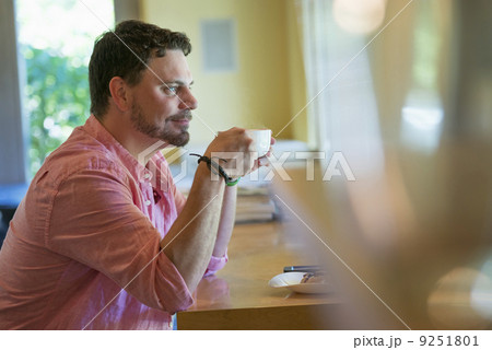 A man sitting at a cafe table, holding a cup of coffee. A man sitting at a cafe table, holding a cup of coffee. 9251801