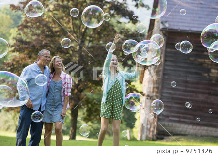 A family sitting on the grass outside a bar, blowing bubbles and laughing. 9251826