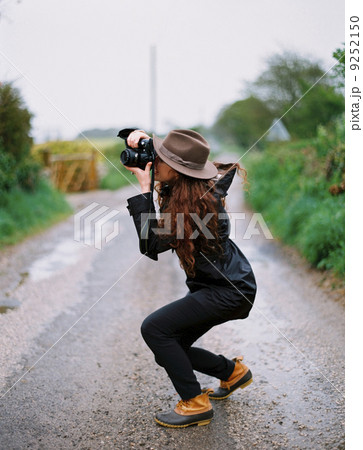 A woman crouching to take a photograph on a country road. 9252150