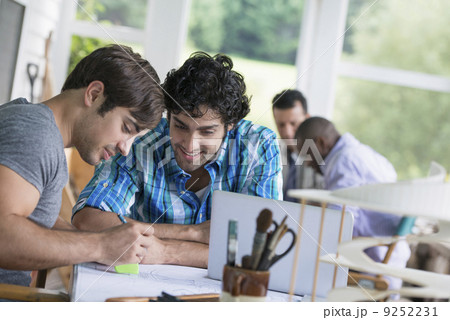 Two men seated, one drawing on paper.  9252231