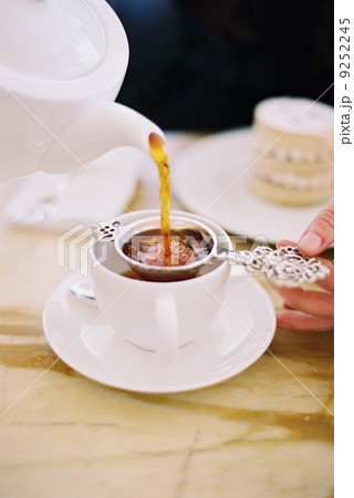 A person pouring a cup of tea, using a strainer. White china. Elegant afternoon tea. 9252245