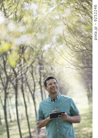 A man standing in an avenue of trees, holding a digital tablet. A man standing in an avenue of trees, holding a digital tablet. 9252246