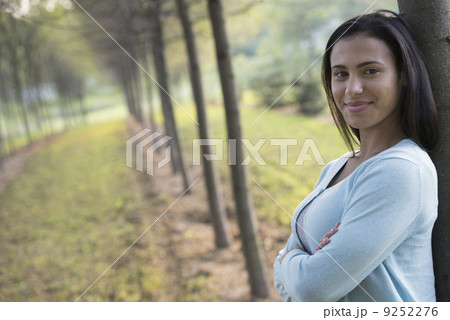A woman with arms folded, leaning against a tree. A woman with arms folded, leaning against a tree. 9252276