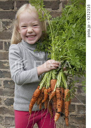 A young girl holding a large bunch of carrots. 9252316