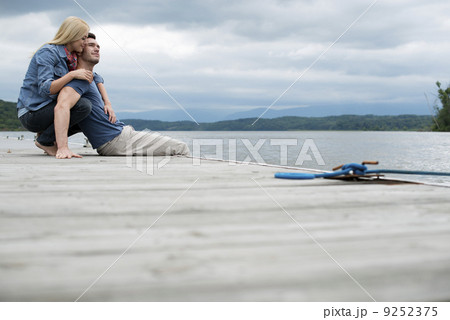 A man and woman seated on a jetty by a lake. A man and woman seated on a jetty by a lake. 9252375