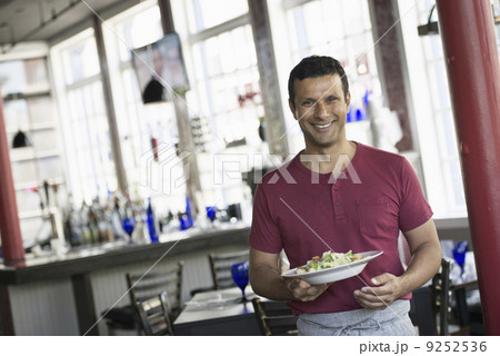 A cafe interior. A man in a waiter's apron serving a meal.  9252536