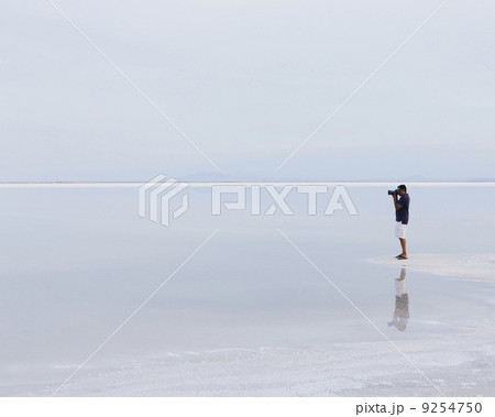 A Man Standing On The Edge Of The Flooded Bonneville Salt Flats, Taking A Photograph At Dusk. 9254750