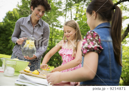 A Summer Family Gathering At A Farm. A Woman And Two Children Standing Outside By A Table, Laying The Table. Making Lemonade. 9254871