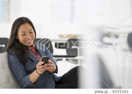 Business. A Woman Seated In A Comfortable Chair, Checking Her Smart Phone For Messages.  9255161