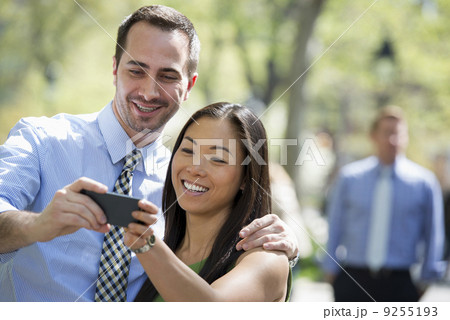 A Couple With A Smart Phone, Side By Side. A Man In The Background. A Couple With A Smart Phone, Side By Side. A Man In The Background. 9255193