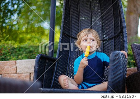 Little blond boy eating yellow ice cream 9331807