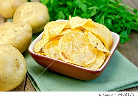 Chips in a bowl with a potato on the board and napkin 9403175